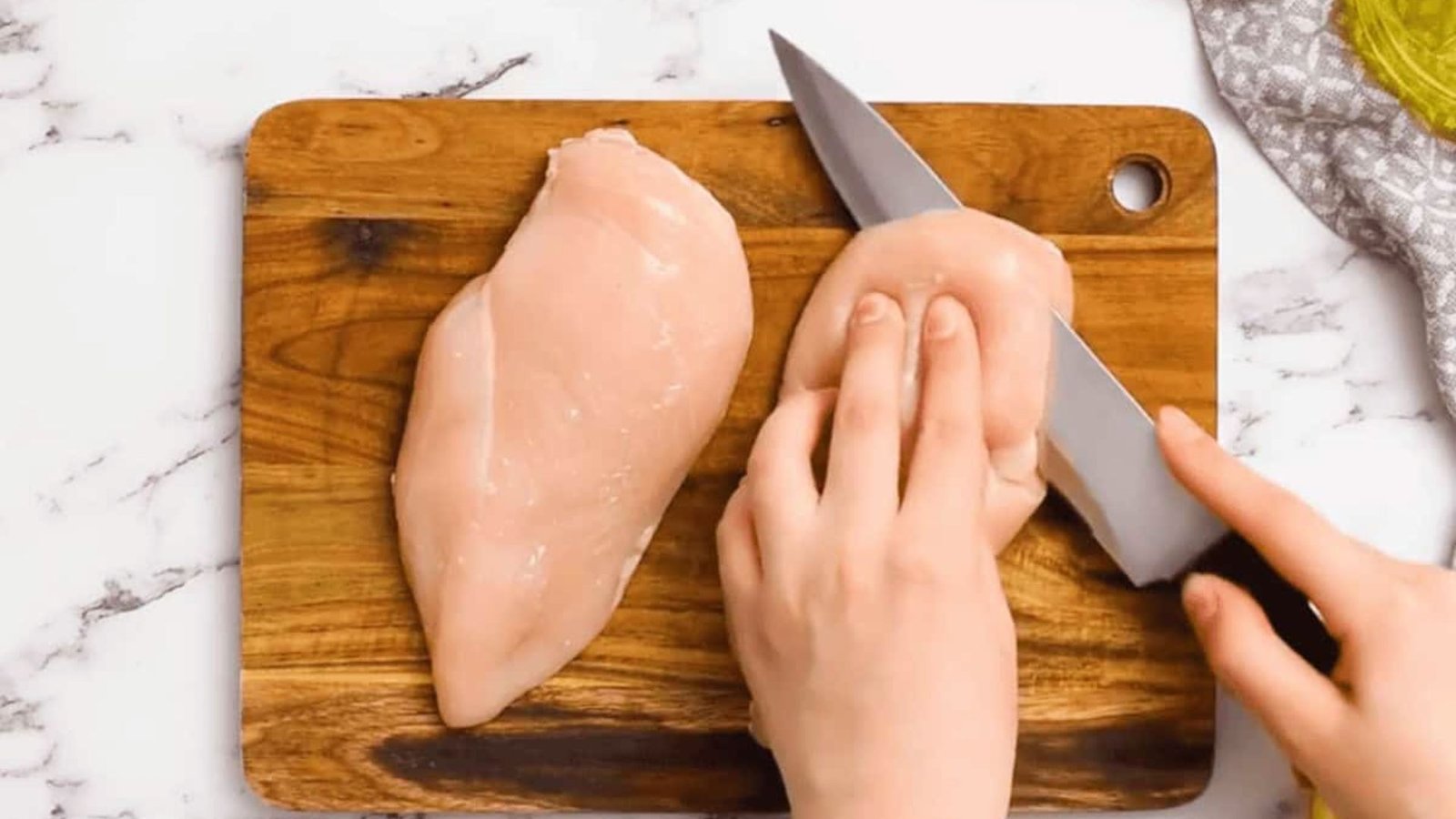 A person slicing chicken cutlets on a wooden cutting board as part of meal preparation.