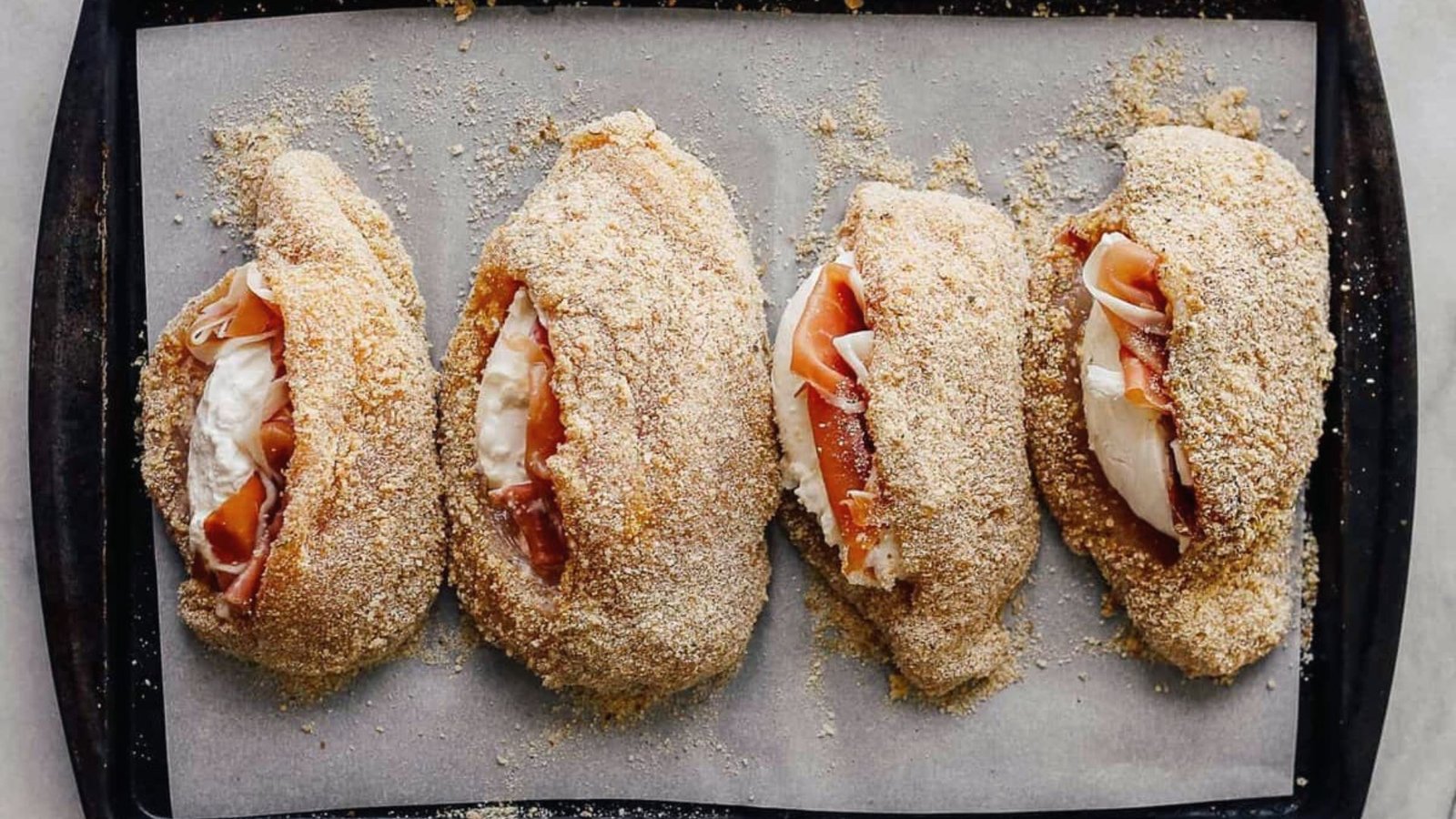 Four stuffed chicken Rollatini filled with prosciutto and cheese, arranged neatly on a baking sheet.