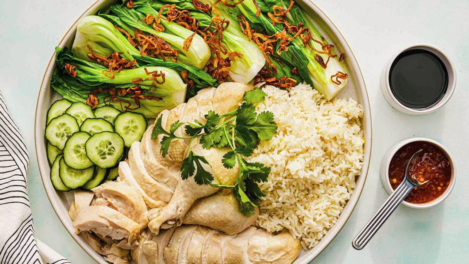 A plate of Hainanese chicken rice featuring tender chicken, cucumber slices, and a serving of white rice.