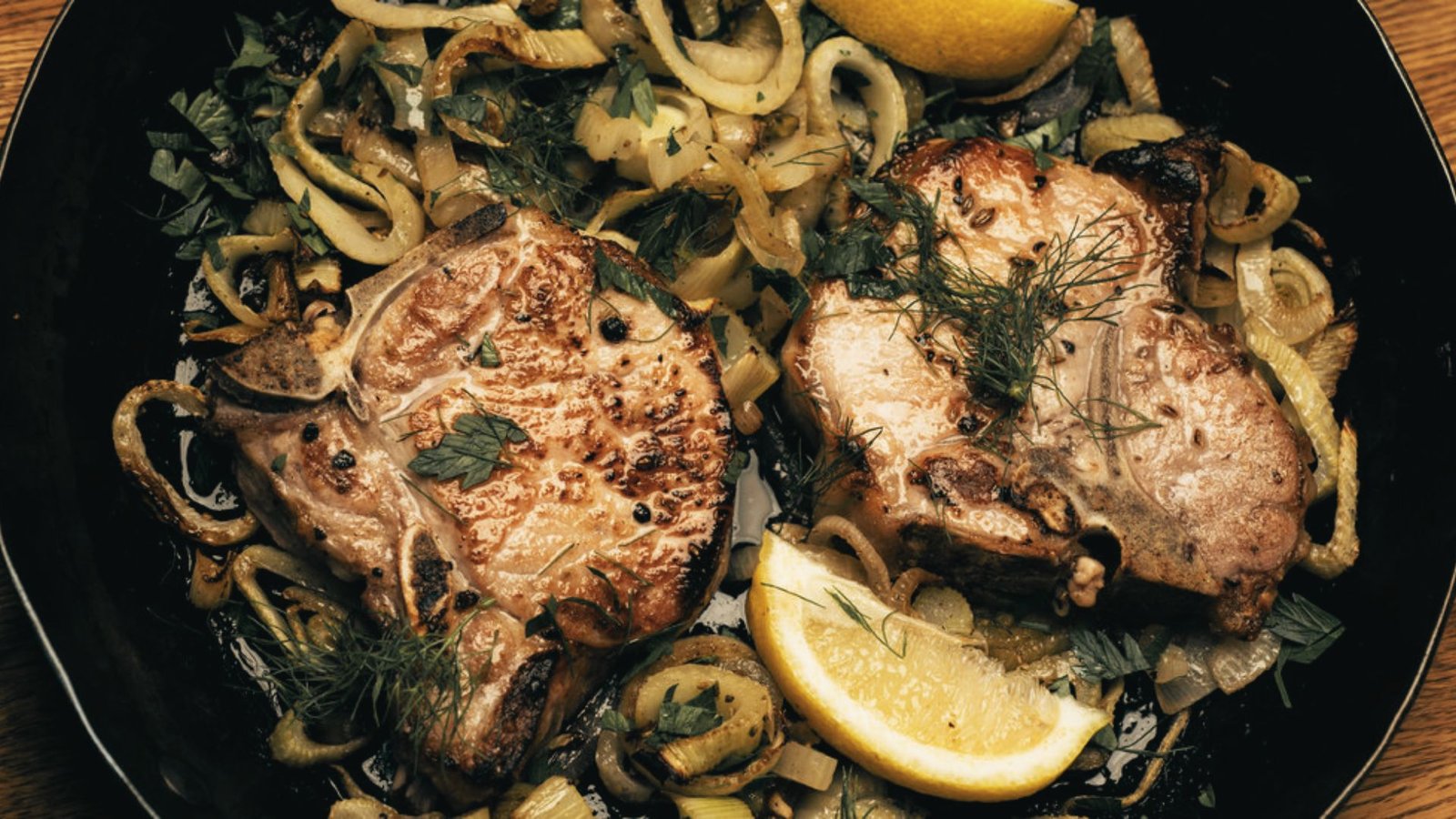 Two pieces of pork with onions and lemons arranged on a black plate, showcasing Pork Brine Recipe with Citrus and Herbs