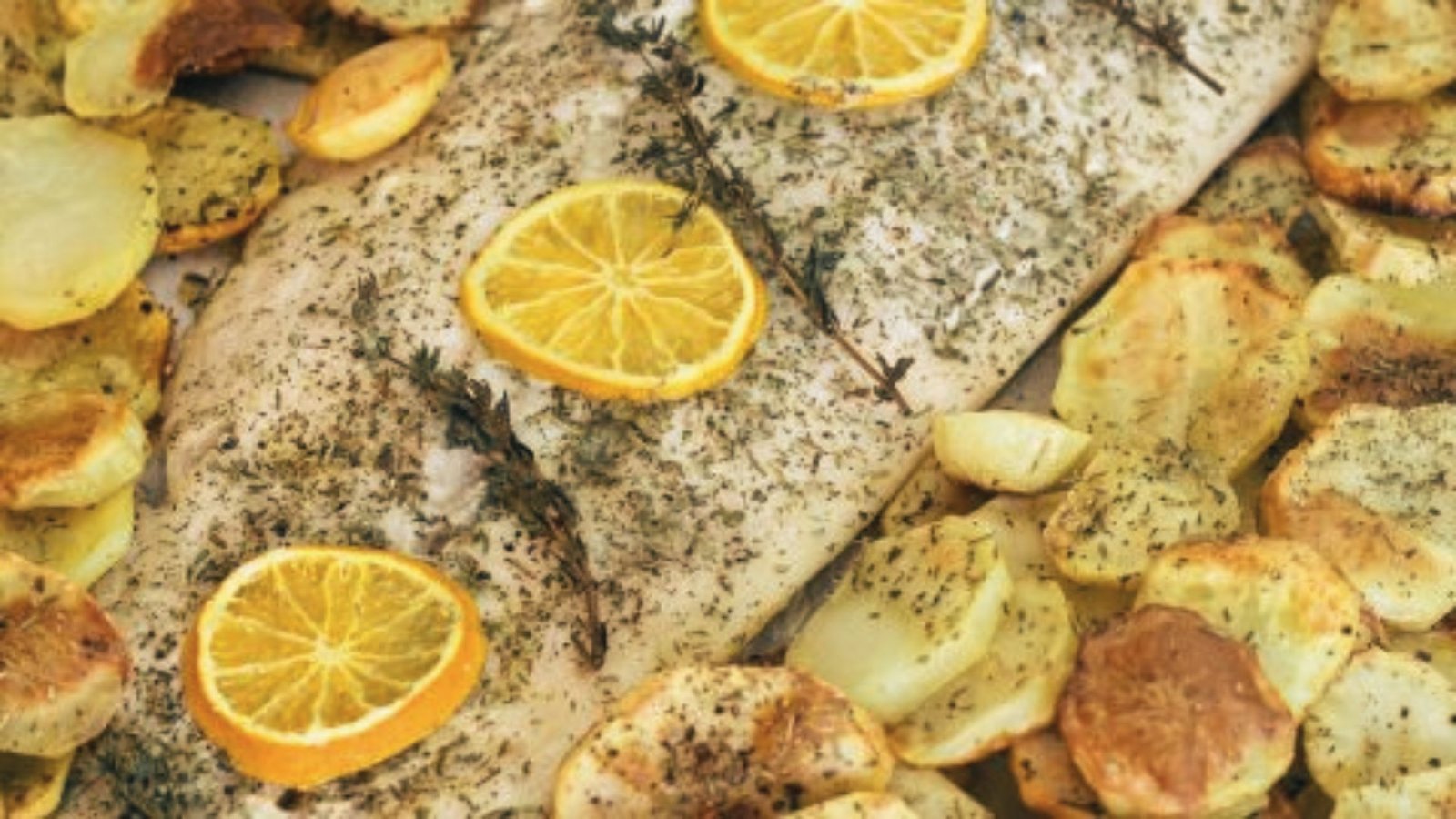 A cooked fish topped with lemon slices and served with golden-brown potatoes on a white plate.