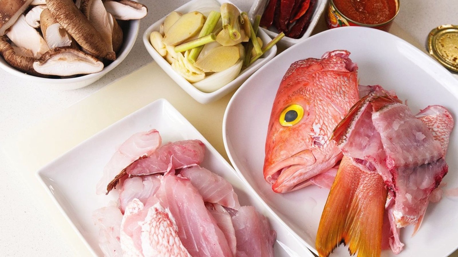 A selection of raw fish and fresh vegetables arranged on a table, ready for a Thai fish recipe preparation.