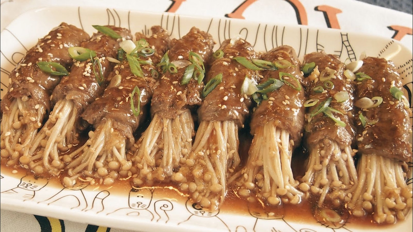 A plate of enoki beef rolls garnished with green onions and served with a dipping sauce.