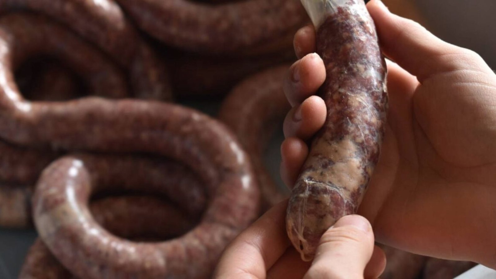 A person holding a sausage in his hand, demonstrating the process of stuffing casings and forming links.