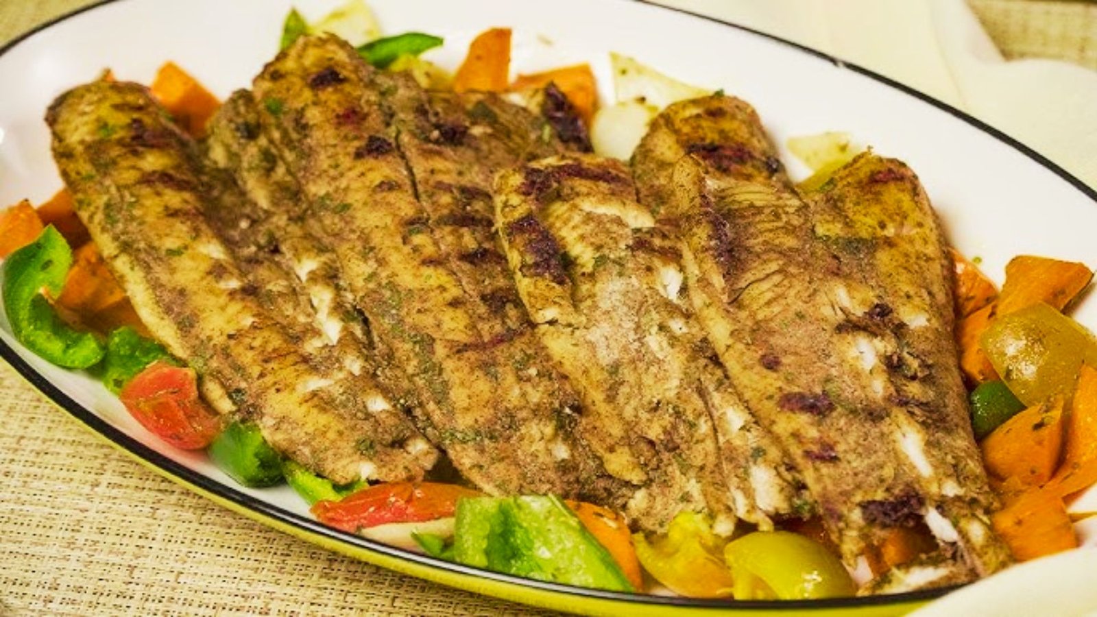 A plate of sweet and spicy grilled catfish served with colorful vegetables, showcasing a caramelized crust from the grill.
