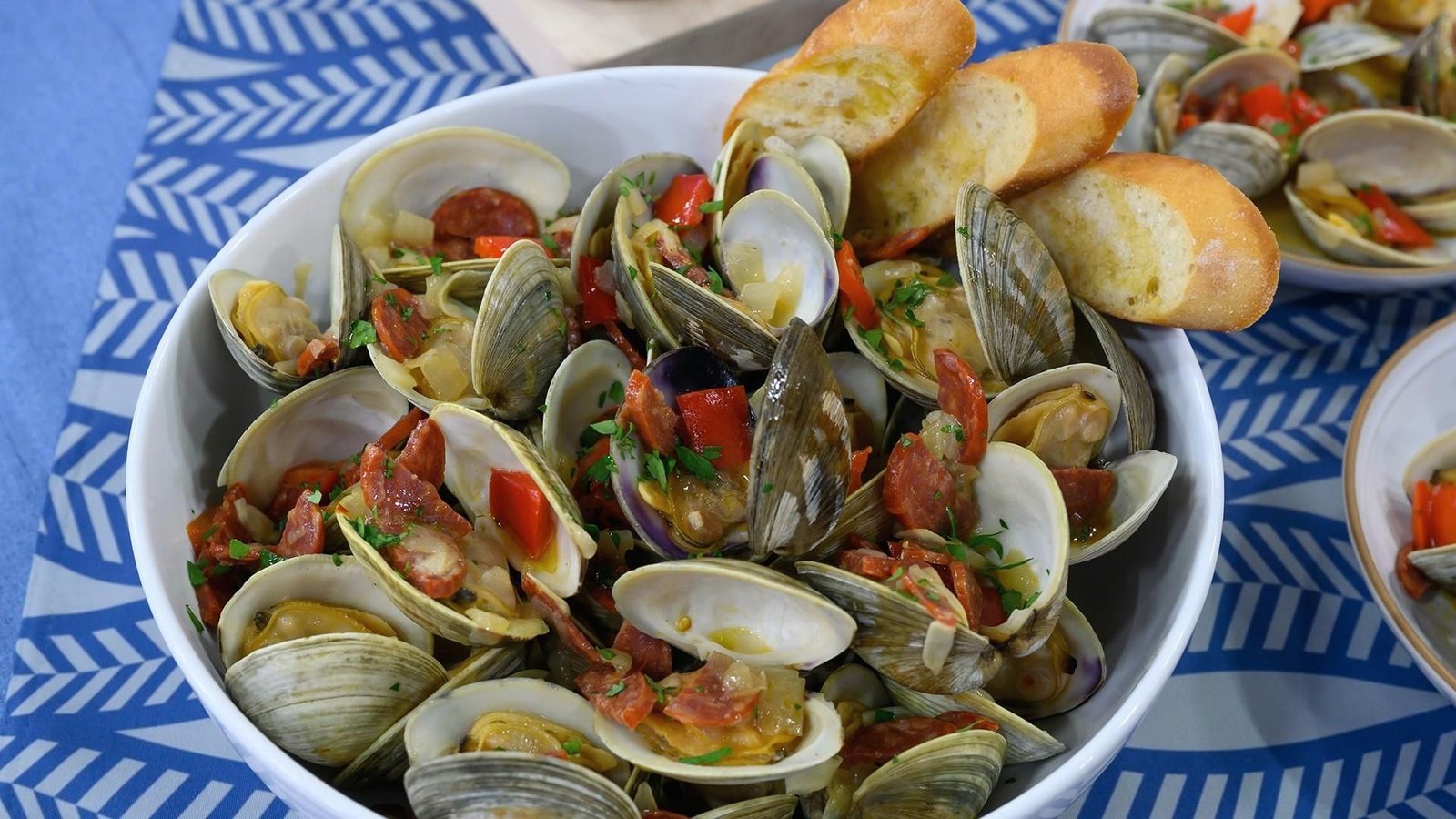 A bowl of little neck clams served with slices of bread and fresh tomatoes, ideal for a seafood meal.