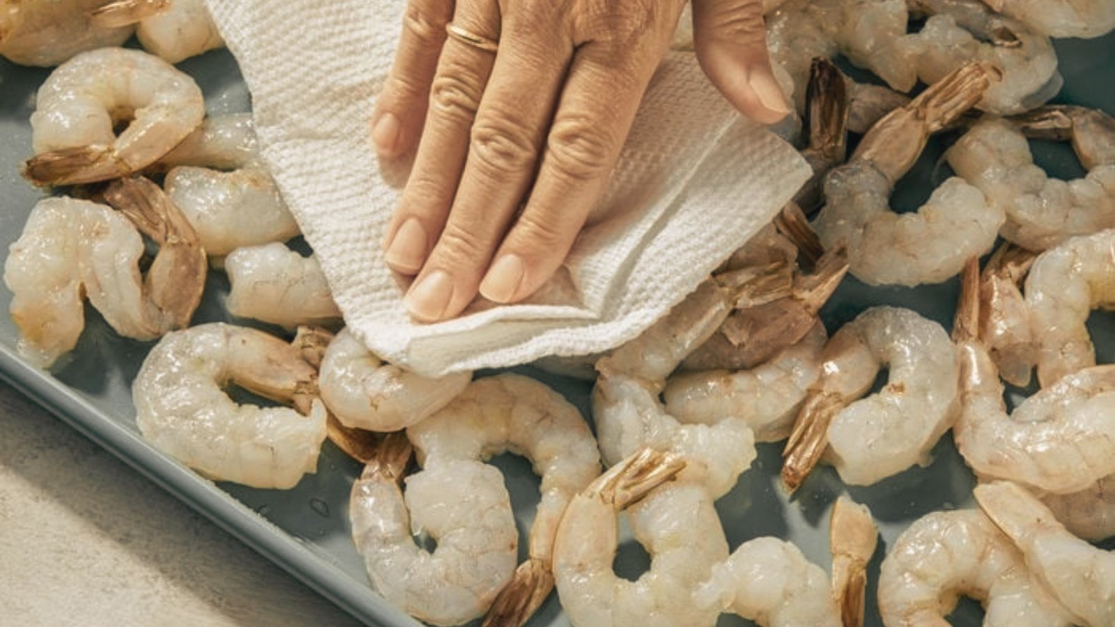 A person carefully wiping shrimp on a tray, demonstrating proper shrimp preparation techniques.