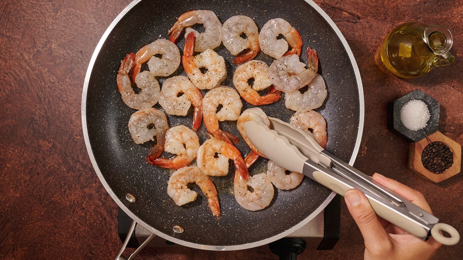 A person holding a spatula over a pan, searing shrimp as part of a cooking process.