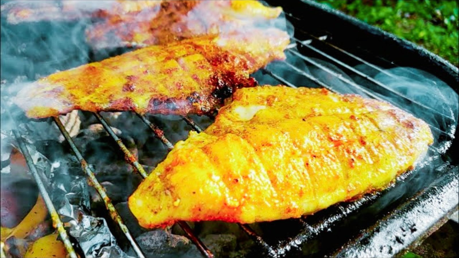 Two fish are cooking on a grill, surrounded by smoke, representing a smoky BBQ style catfish dish.
