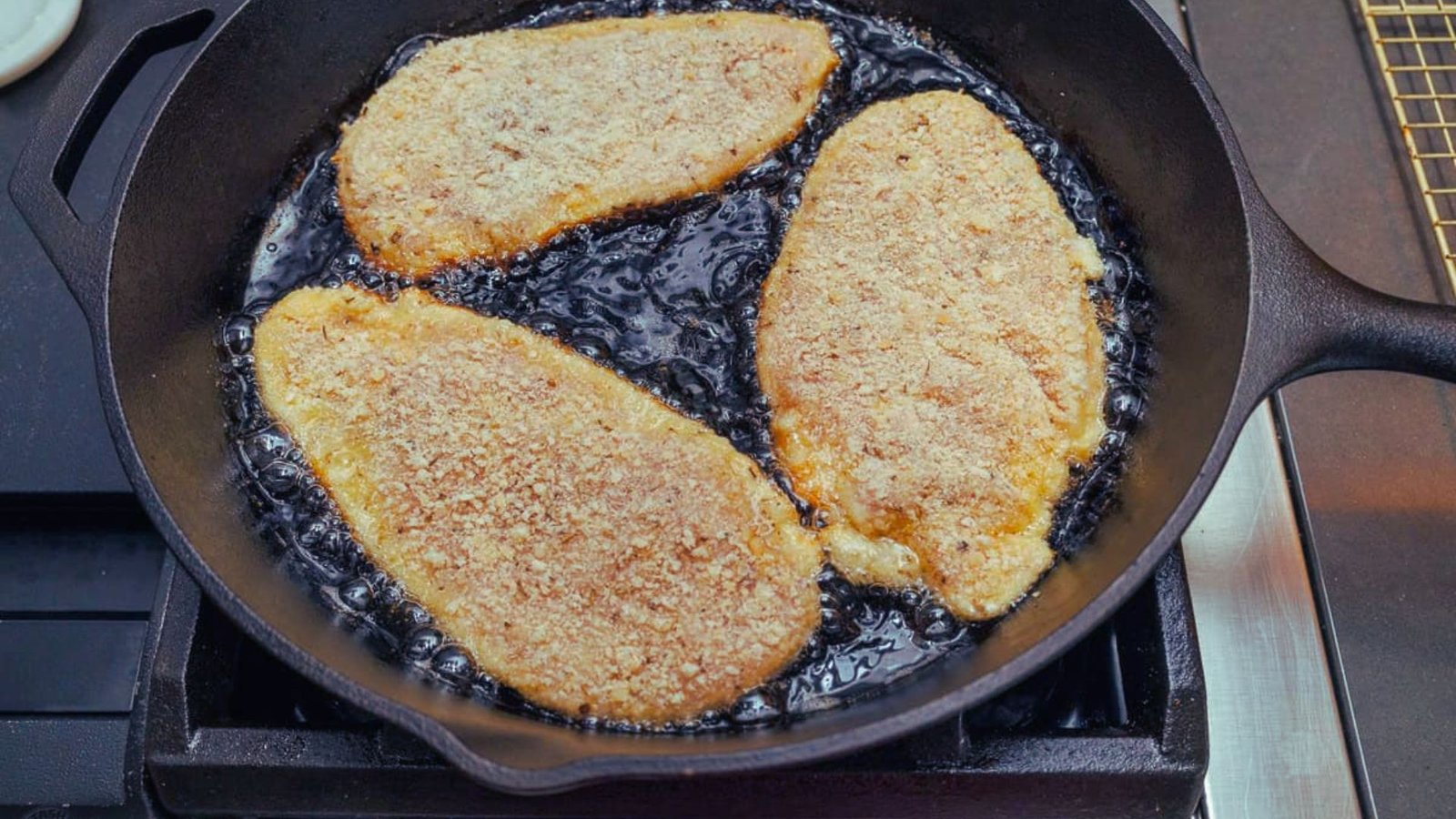 Three pieces of chicken sizzling in a skillet, cooking until golden and crispy.