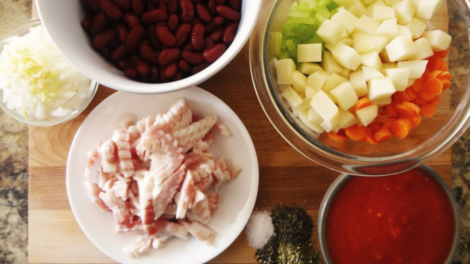 Ingredients for a Beef Minestrone Soup, including chicken, beans, vegetables, and spices arranged on a wooden surface.