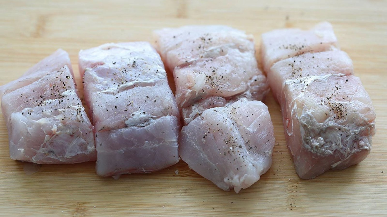 A cutting board displaying raw fish pieces, indicating the initial step in meal preparation.