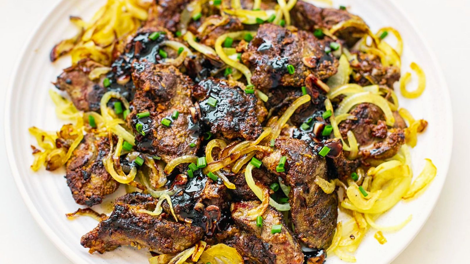 A dish of pan-fried chicken livers accompanied by onions, presented on a dining table.
