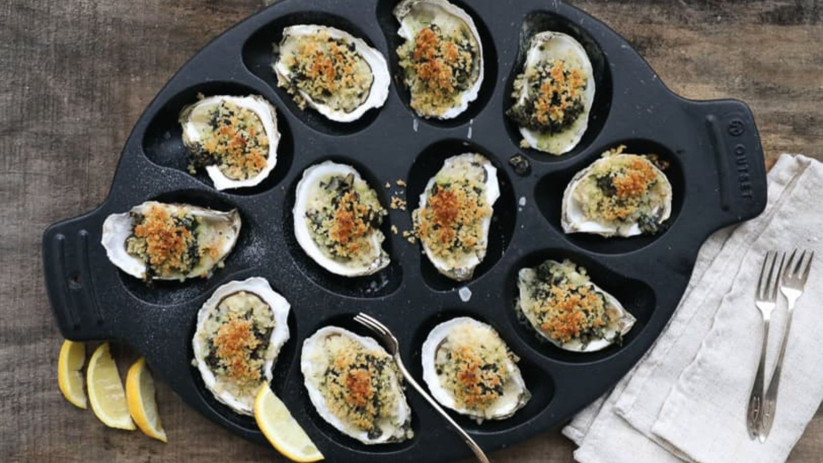 A pan filled with fresh oysters and lemon wedges, showcasing an Oyster Rockefeller.