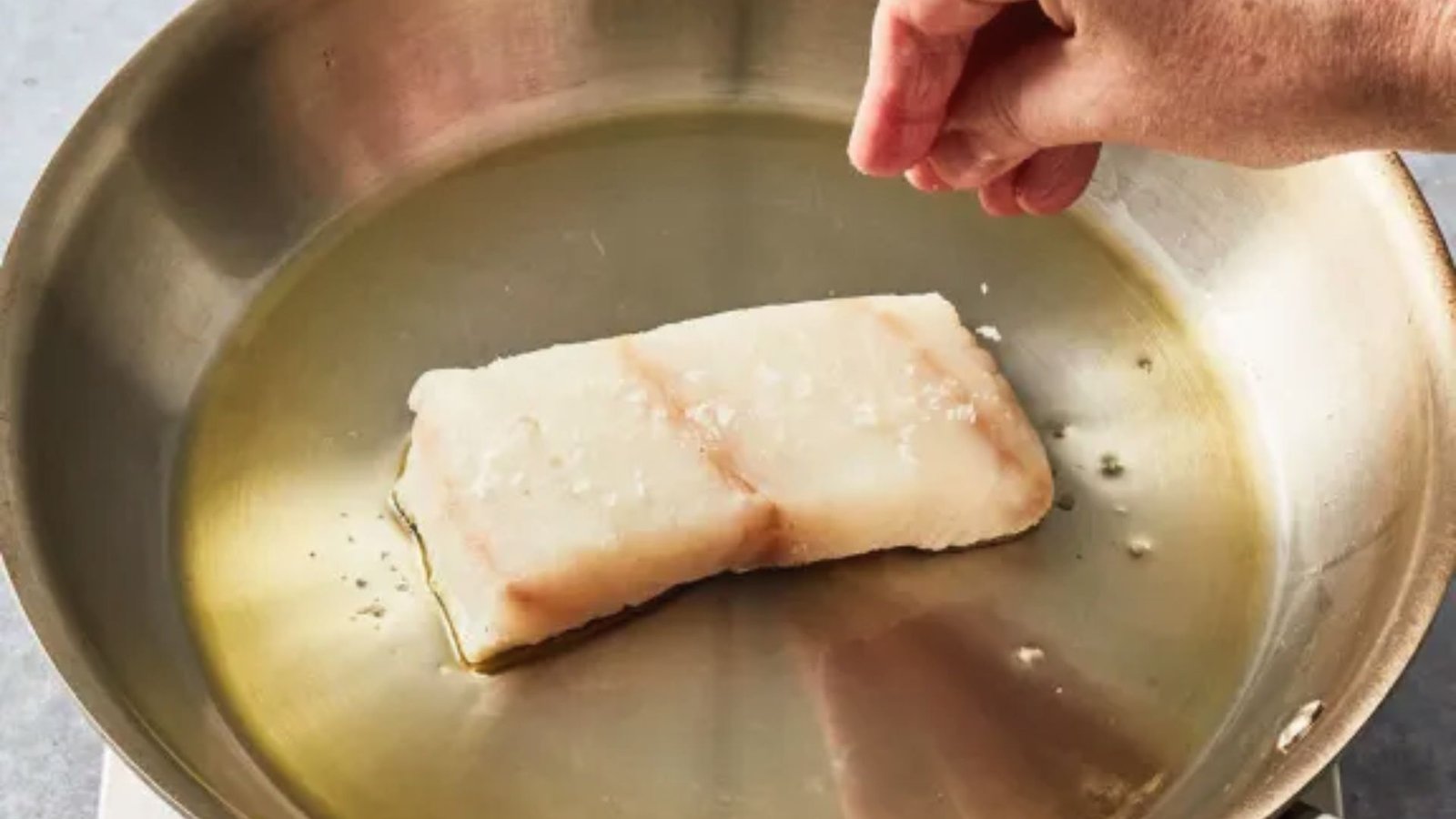 A person cooking fish in a pan on a stovetop.