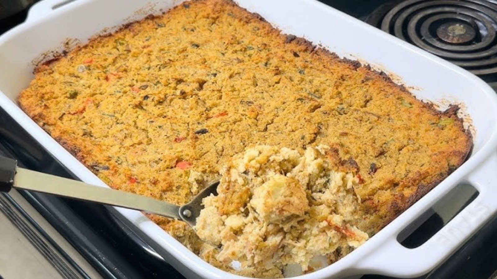 A casserole dish filled with chicken dressing and a spoon resting inside, highlighting a delicious recipe.