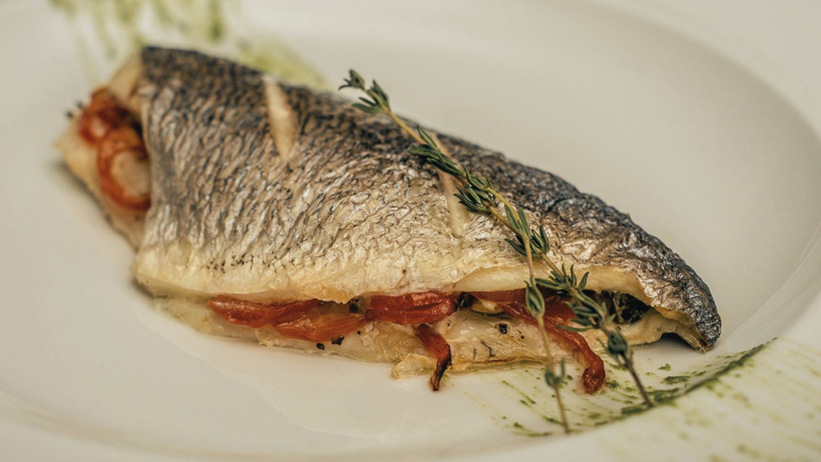 A cooked fish garnished with fresh herbs on a white plate, highlighting a healthy autumn meal option.