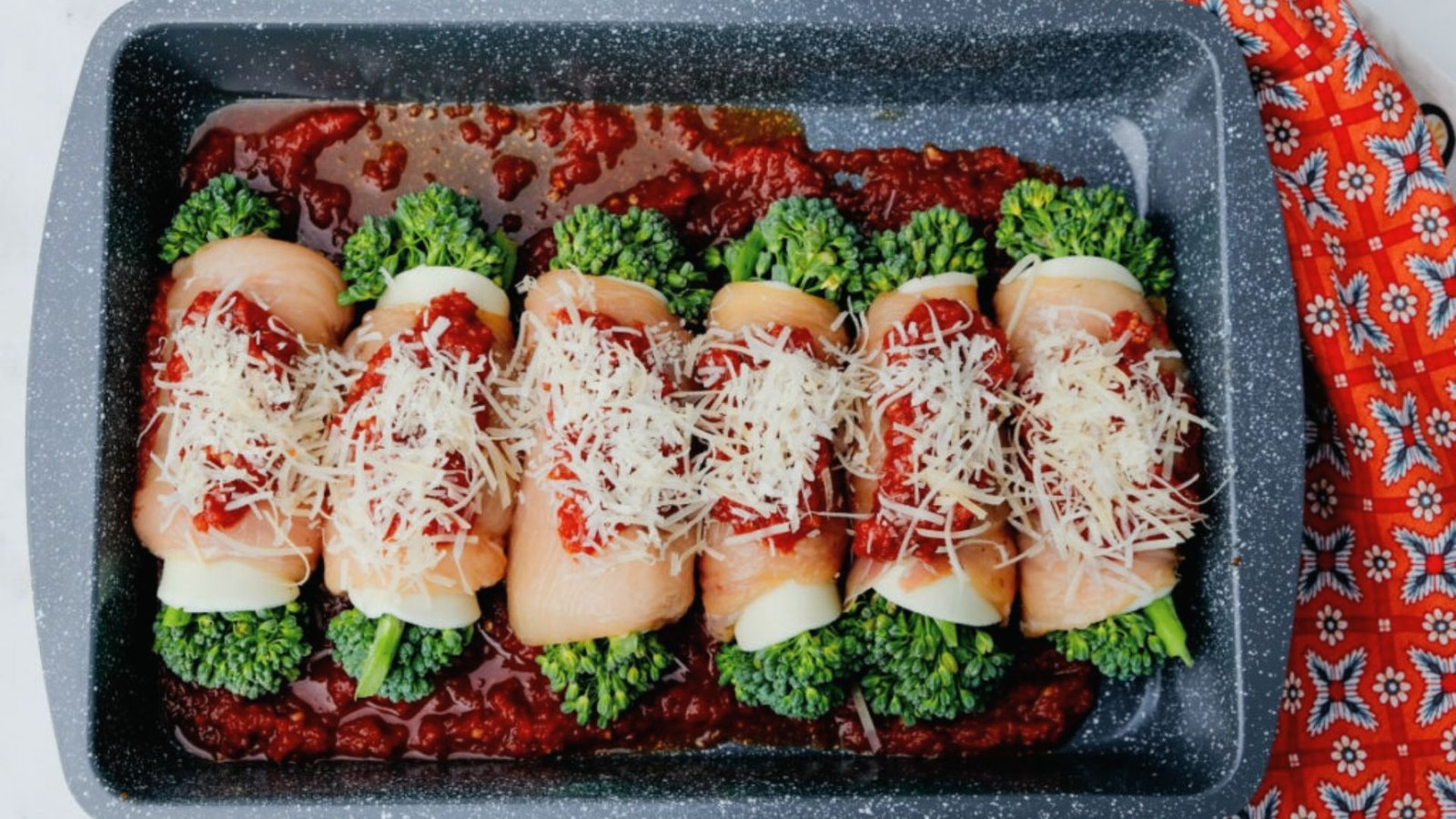 A casserole dish filled with rolled chicken Rollatini and melted cheese, ready for baking as part of the cooking process.