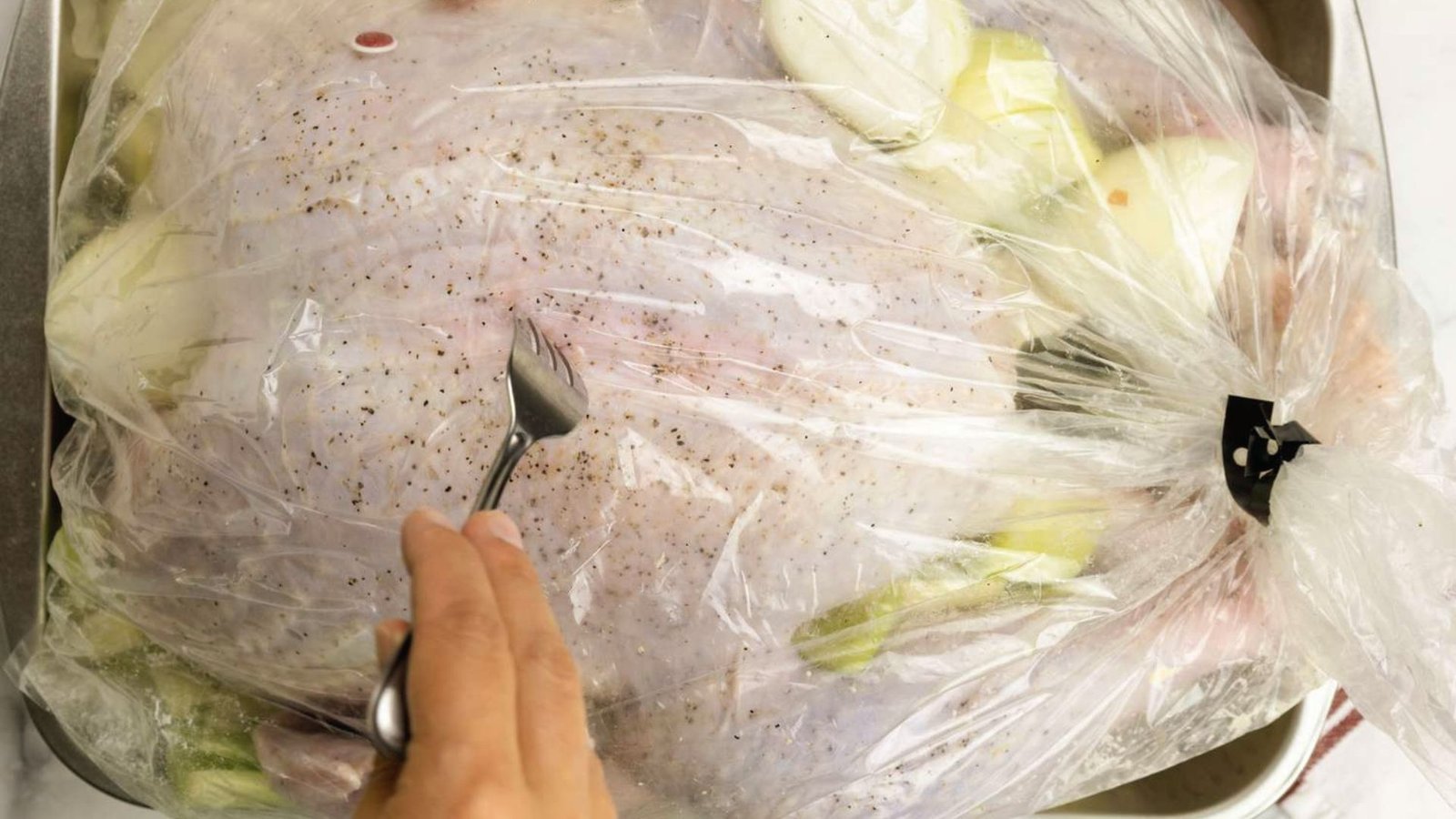 A person slicing into a turkey wrapped in plastic, demonstrating the process of sealing it in a bag for storage.