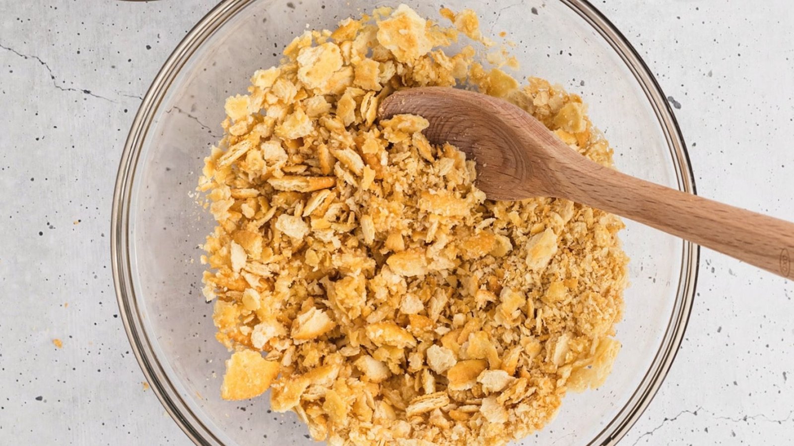 Crushed crackers in a big transparent bowl mixed with butter.