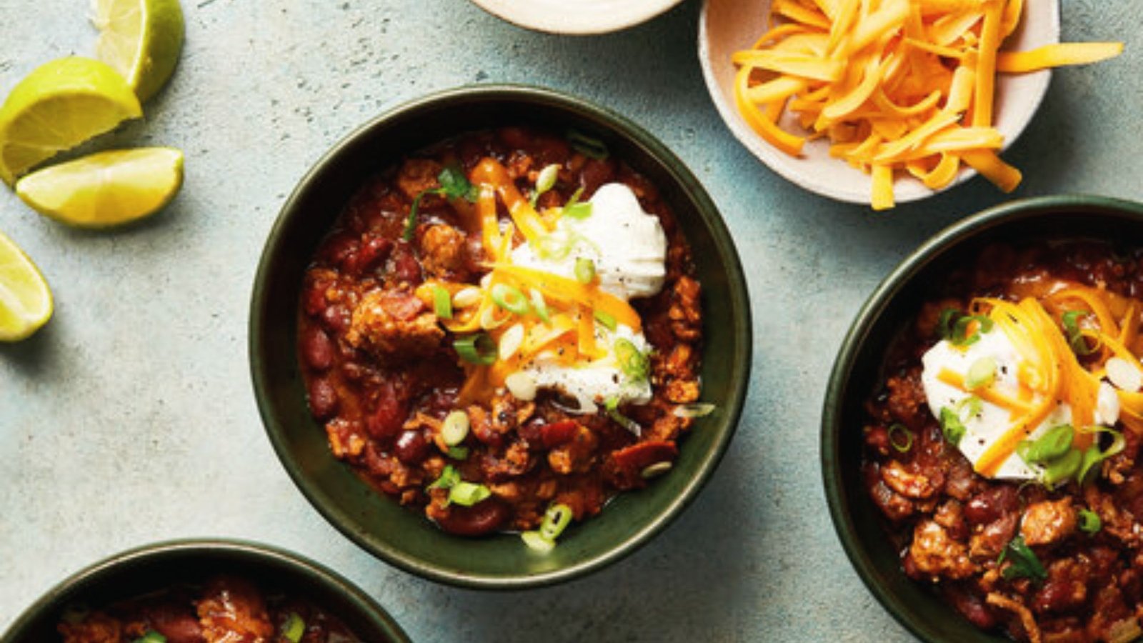 Three bowls of turkey chili topped with cheese and sour cream, showcasing a hearty and flavorful dish.