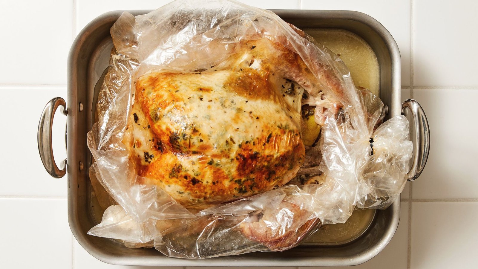 A whole chicken wrapped in plastic sits in a pan, ready for cooking using a turkey in a bag recipe.
