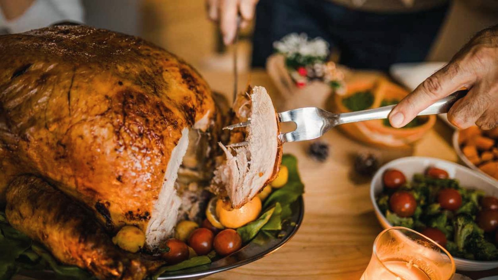A person carves a turkey on a table, preparing it for serving after allowing it to rest.
