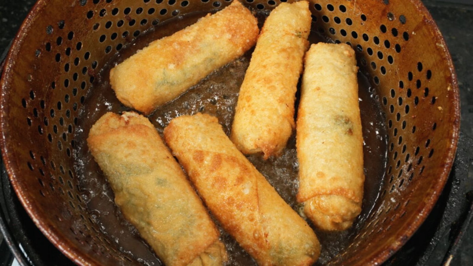 A basket of fried food sits on a stove top, with oil heating nearby, ready for cooking.