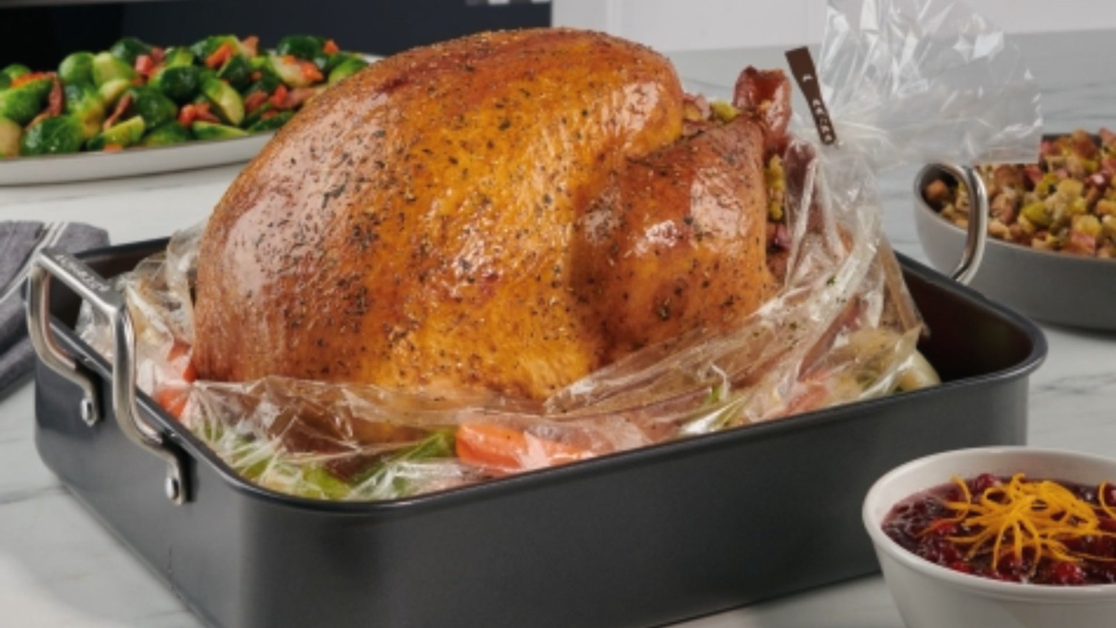 A whole turkey wrapped in plastic sits on a kitchen counter, ready for proper roasting preparation.