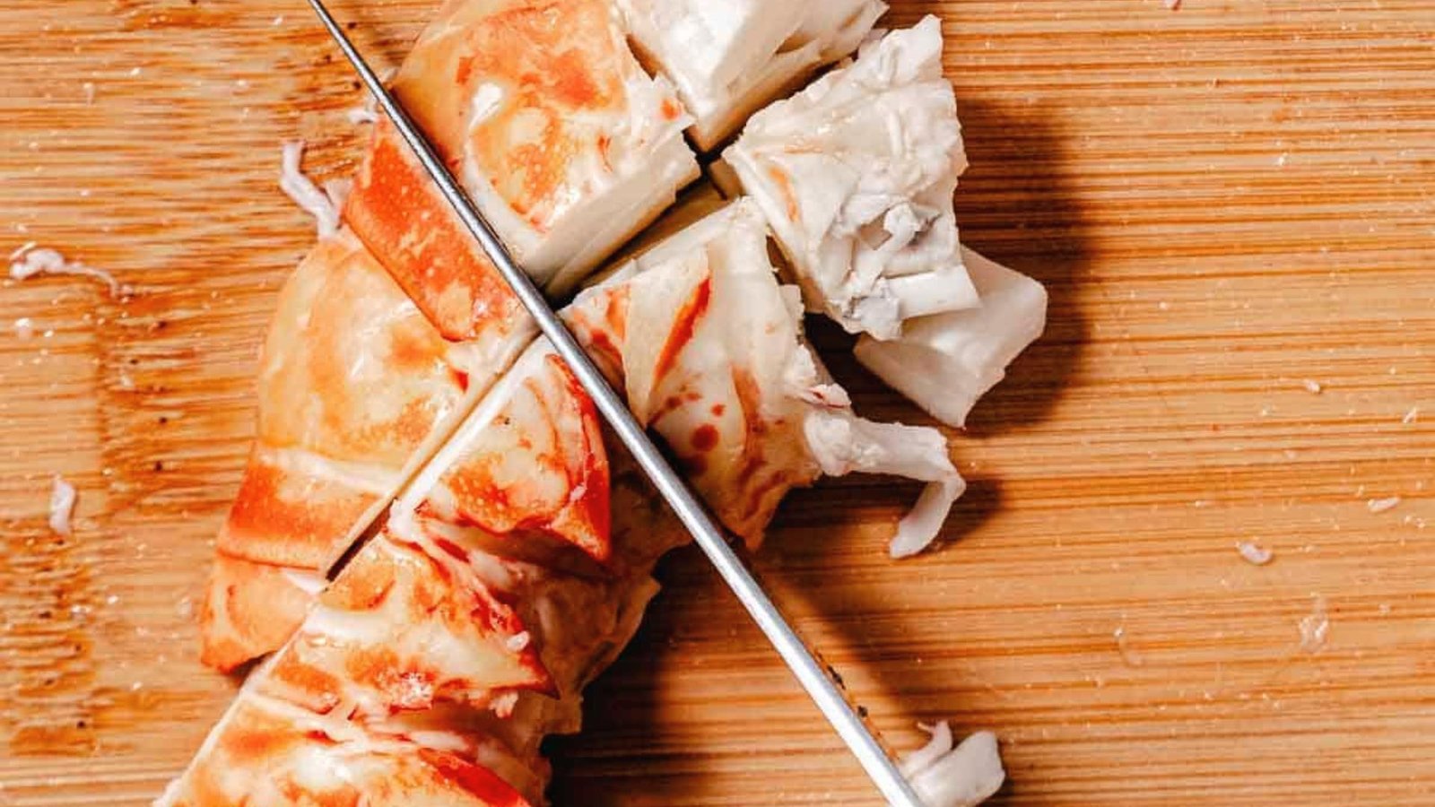 A knife cuts a lobster into perfect bite-sized pieces on a cutting board.
