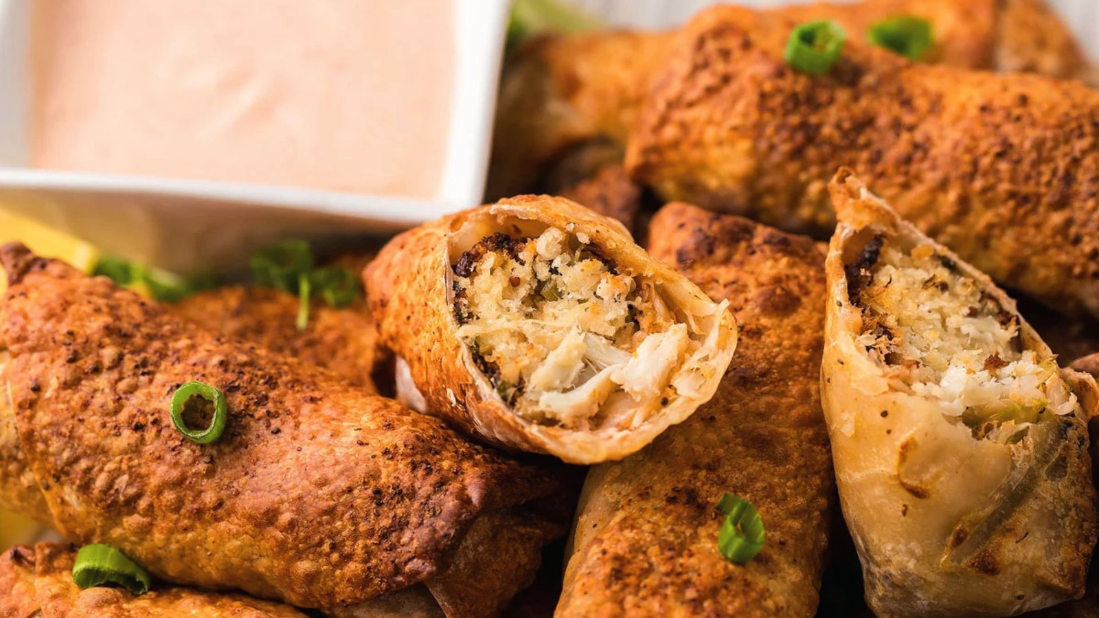 A plate of crispy crab egg rolls served with a flavorful dipping sauce.