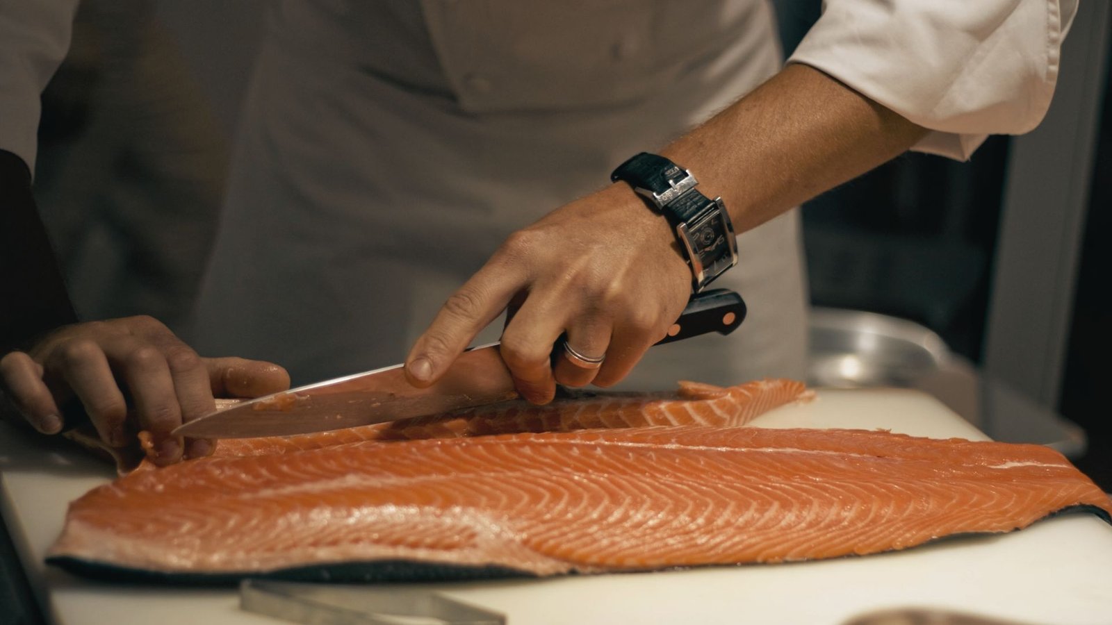 A chef skillfully cuts a salmon fillet on a wooden cutting board, preparing it for cooking.