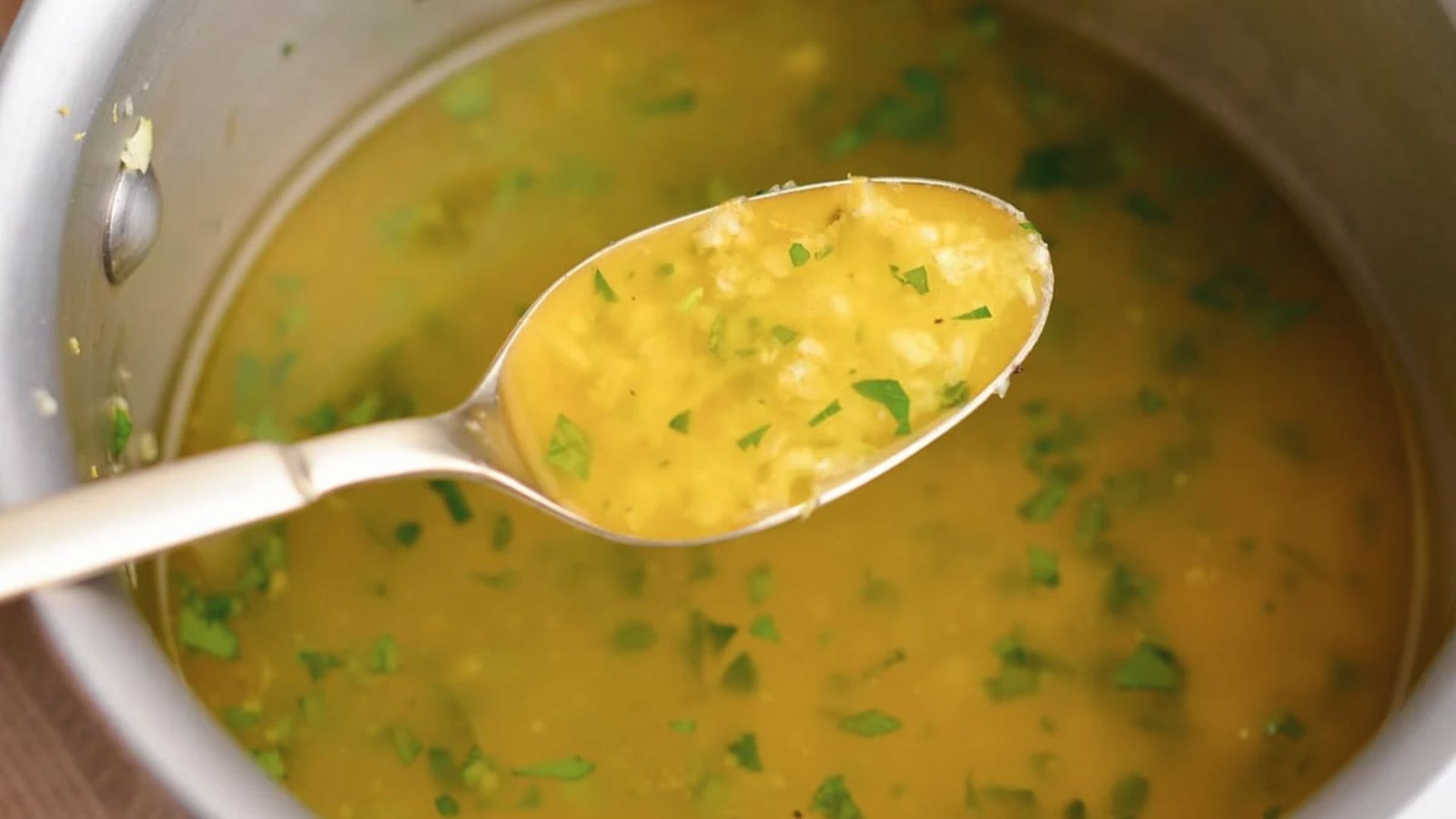 A spoonful of sauce being lifted from a pot, illustrating the preparation of garlic butter sauce.