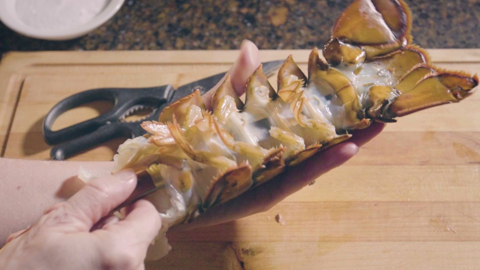 A person holding a lobster with a knife, demonstrating how to easily de-shell lobster tails.
