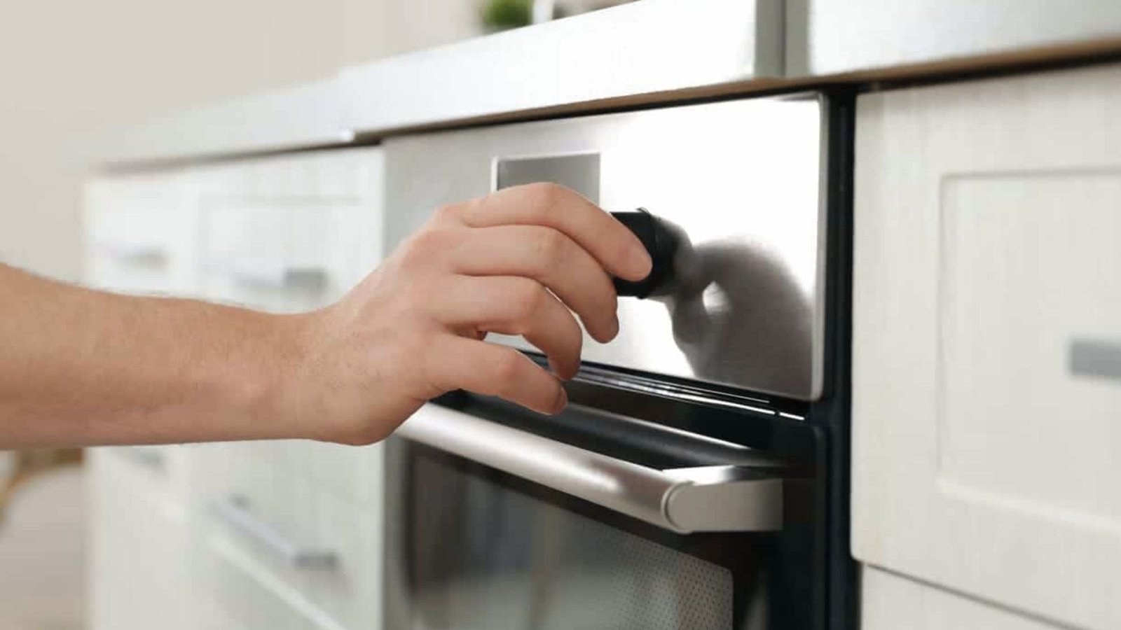 A person opens the oven door with their hand, preparing to preheat it to 350°F.