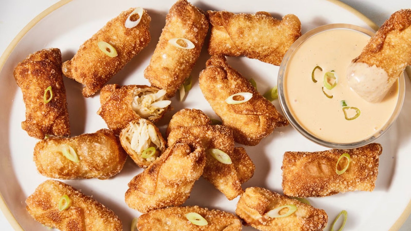 A plate of crab egg rolls served with a small bowl of dipping sauce.