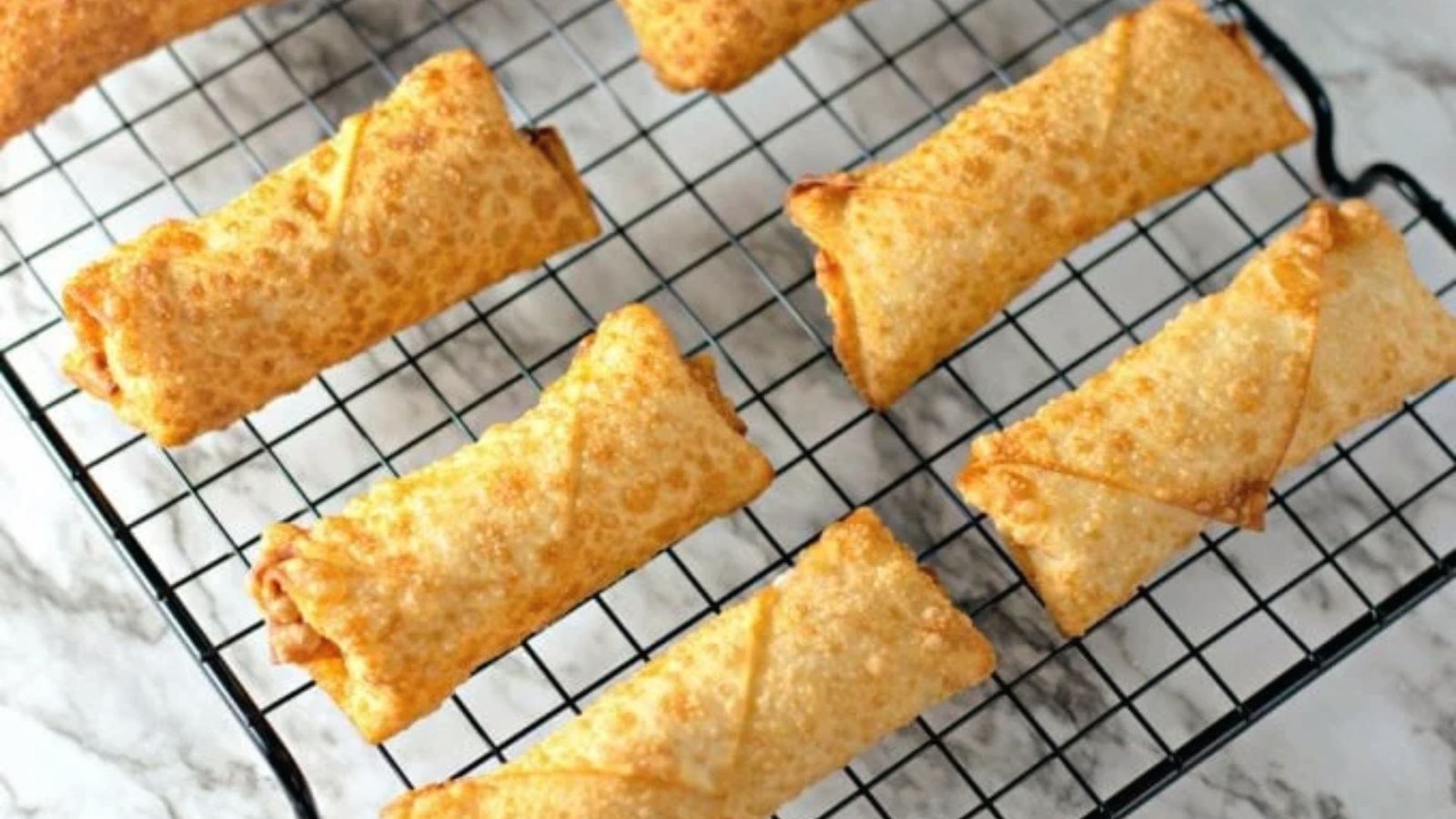 Fried crab egg rolls cooling on a rack, ready to be drained and served.
