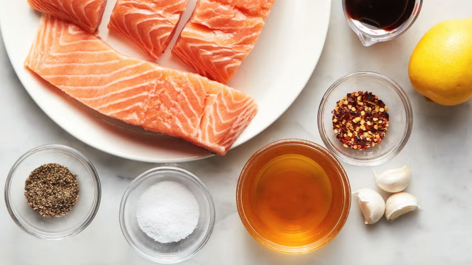 A white plate featuring salmon, garlic, lemon, and various ingredients for a hibachi salmon recipe.