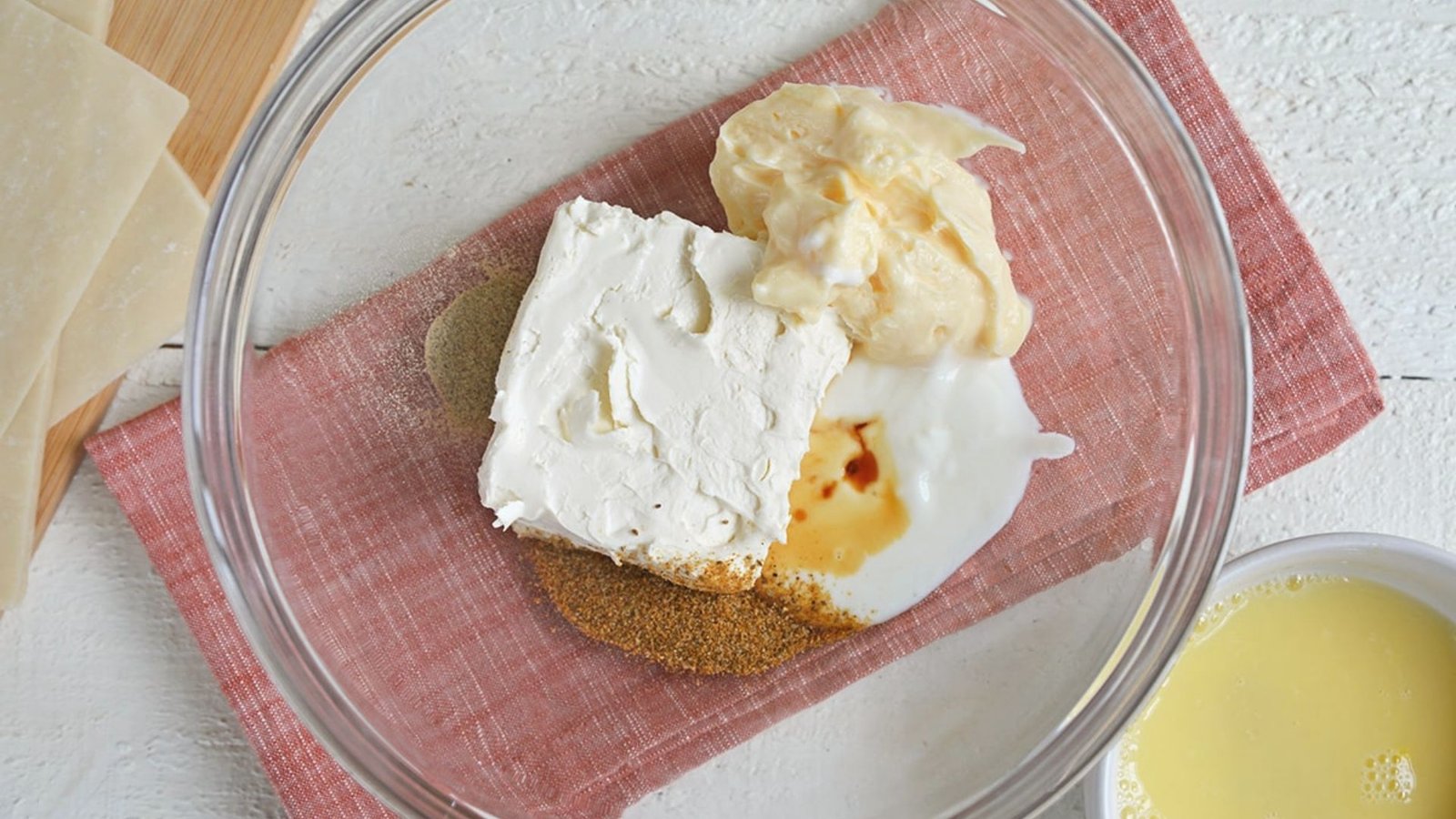 A bowl containing cream cheese, butter, and sugar is placed on a pink cloth, signifying the filling preparation process.