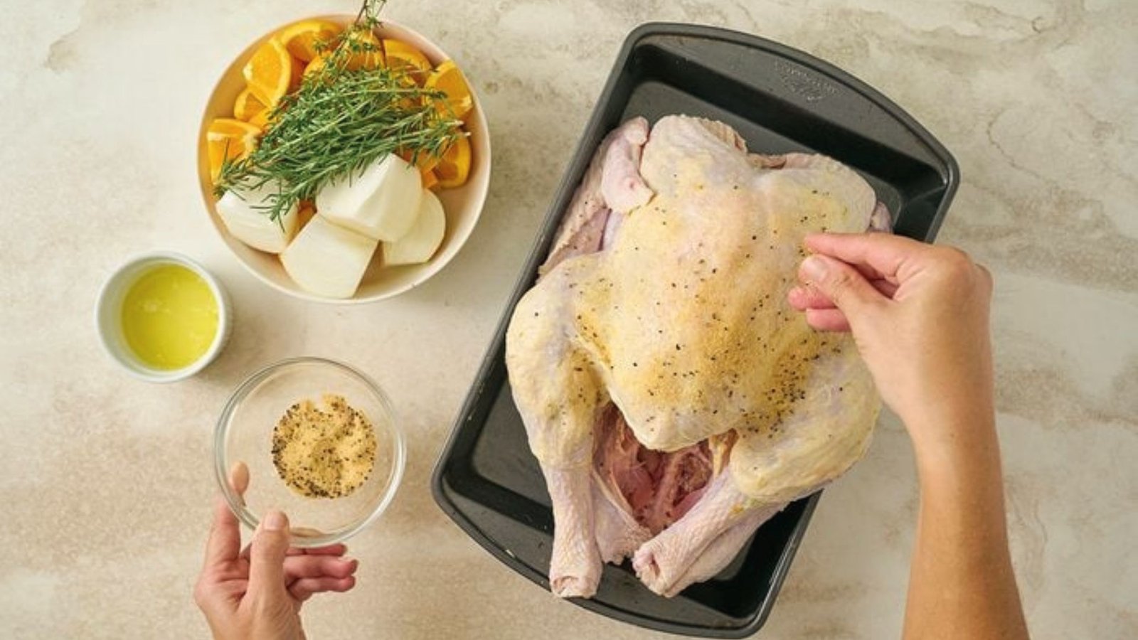 A person seasons a chicken inside and outside while preparing it on a baking pan.