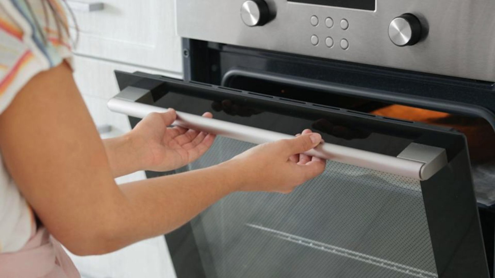 A woman opens the oven door to prepare for cooking chicken.