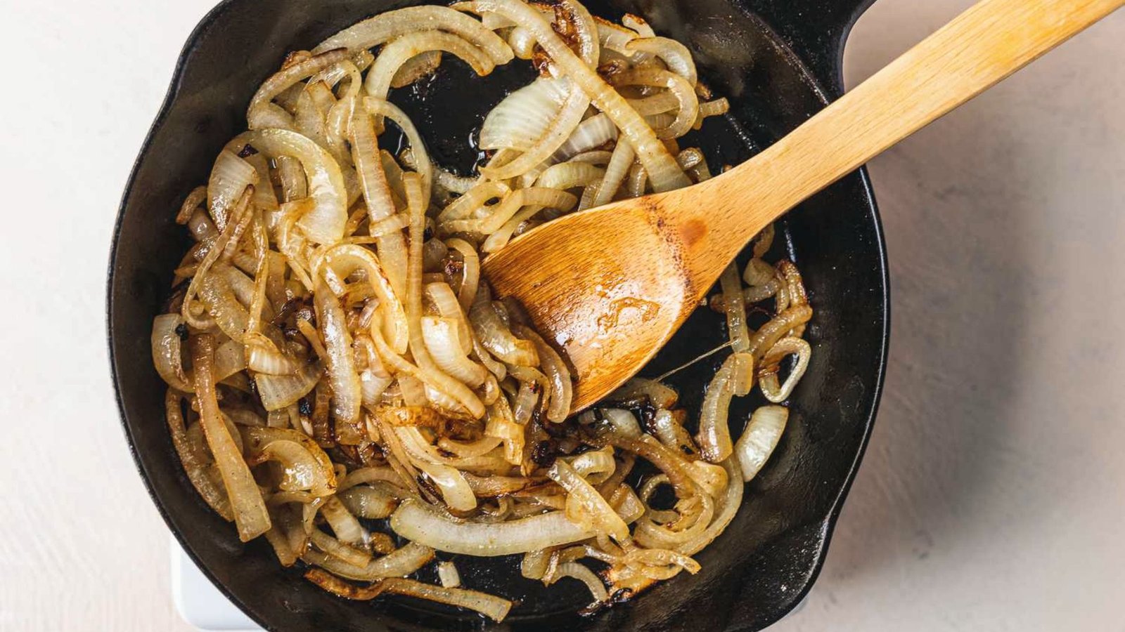 A skillet filled with sautéing onions and a wooden spoon, illustrating the process of building flavor in cooking.